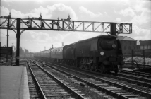 Digital image copy at 800 dpi of an original black and white print photograph retained by donor of Mike Peart, showing a Battle of Britain class locomotive 34080 "74 SQUADRON" under the signal gantry at Eastleigh Station with train from Bournemouth to Waterloo.