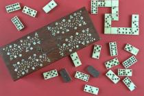 Dominoes, wooden box with hinged lid inlaid with a mother of pearl floral design, and a metal handle and lock, containing a double nine set of bone dominoes, the dominoes are white on top of black bases and are held together by a either a central brass 