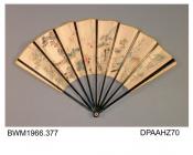 Fan, paper leaf painted with oriental scene of exotic birds, monkeys, goldfish and two figures, one of whom is wearing a white fur jacket, plain black lacquered sticks and guards with etched detail, reverse cream with gold flecking, narrow outer border 