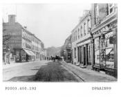 Black and white photographic enlargement of postcard showing view looking east along London Street, Basingstoke, to left is shop and premises of Harry Edmund Powell, pianoforte, organ, harmonium and music warehouse, with Red Lion Hotel beyond, on right 