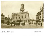 Sepia postcard showing view looking north towards Town Hall, Market Place, Basingstoke, in centre are two soldiers with two horses pulling field gun magazines, alongside is the electric lamp post, to right is a barrow or hand cart stood on end, several 