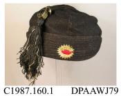 Hat, schoolgirl's, Andover Grammar School, black wool, four segment crown trimmed with large black and cream silk tassel, turned up front and back brim sections trimmed top-stitching, school emblem of red hand against yellow sunburst embroidered on front