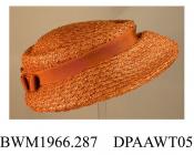 Hat, women's, light tan synthetic straw, low crown trimmed tan petersham band with flat bow at rear, shaped medium brim, inner band of narrow brown petersham, unlined, round black elastic to hold on head, approximate length 240mm, approximate height 100