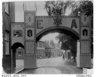 Black and white photograph showing view looking west along Winchester Street, Basingstoke from Winchester Road, in the foreground a temporary archway has been erected to celebrate the coronation of Edward VII in June 1902, there are photographs of the K