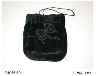 Bag, black velvet, front trimmed with bow in black beads, cuff lined with light brown silk, bag lined black, black plastic rings attached internally and having black cord drawstring, approximate width 165mm, approximate depth including cuff 205mm, c1880