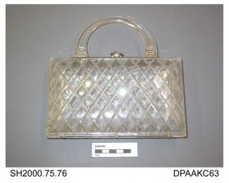 Handbag, rigid transparent acrylic, incised grid design on both sides, with inset imitation diamonds on the front face, lever closure with large imitation diamond knob, unlined, white metal frame with plain single rigid acrylic handle, American, approxi
