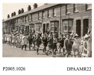 Photograph, black and white, showing local children marching throught the streets, in honour of King George V Silver Jubilee, Basingstoke, Hampshire. 1935