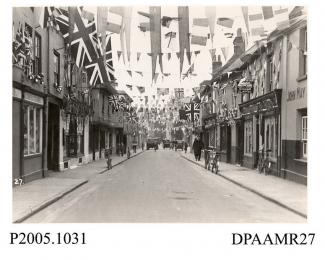 Photograph, black and white, showing decorated shops, in honour of King George V Silver Jubilee, Lower Church Street, Basingstoke, Hampshire. 1935