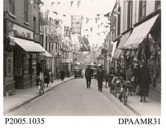 Photograph, black and white, showing decorated shops, in honour of King George V Silver Jubilee, Upper Church Street, Basingstoke, Hampshire. 1935