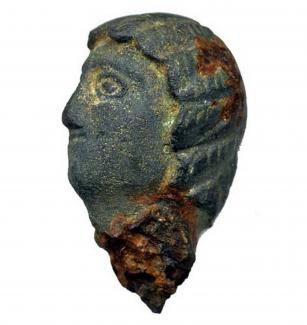 Fragment of a Roman cast copper-alloy and iron possible furniture fitting in the form of a female head, perhaps Julia Domna. The hairstyle is very well defined with a waved, coiffed fringe with six sections either side of the centre, a centre parting on