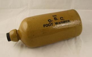 Stoneware hot water bottle, inscribed THE D.B.C. FOOT WARMER, purchased early in the twentieth century by the donor's mother from the Domestic Bazaar Company, The Piazza, Winchester. Original Bakelite screw stopper included.